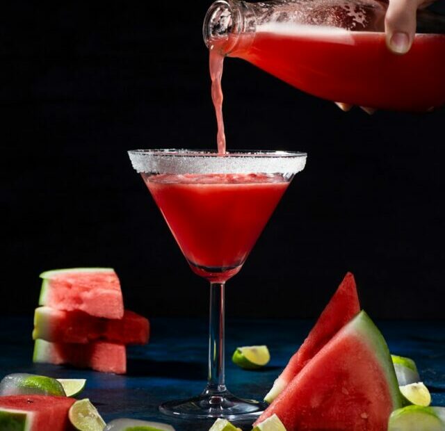 a person pouring a drink into a martini glass