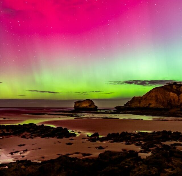 an aurora bore over a rocky beach under a purple sky